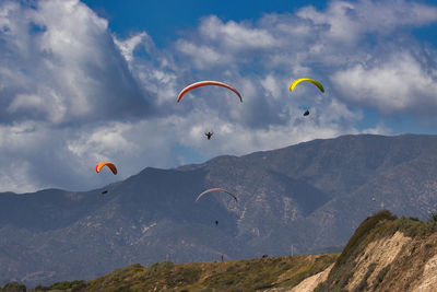 Low angle view of people paragliding against sky