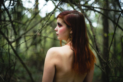 Rear view of topless woman standing in forest