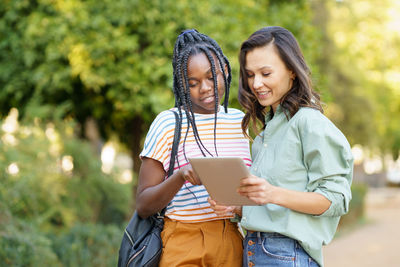 Smiling young women holding digital tablet standing outdoors