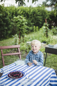 Smiling boy looking away while sitting at dining table in backyard