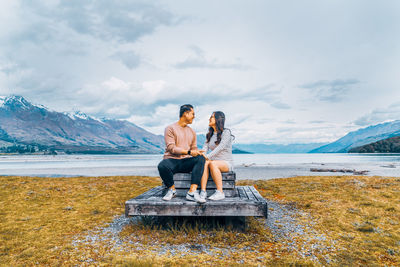 Young couple sitting on shore against sky