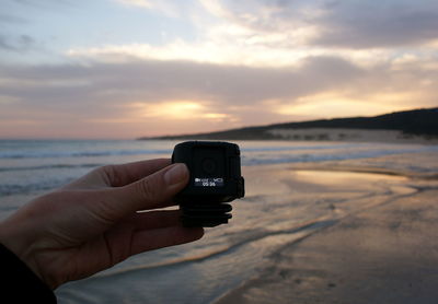 Close-up of hand holding digital viewfinder at beach during sunset