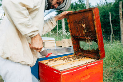 Side view of beekeeper examining beehive on land