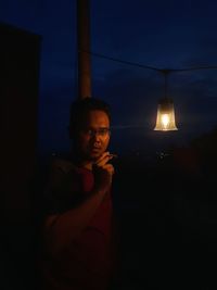 Portrait of young man holding illuminated lamp at night