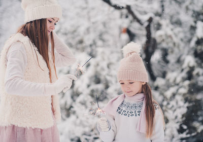 Playful sisters holding sparkler during winter