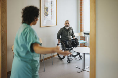 Man in wheelchair looking at nurse gesturing at doorway of waiting room