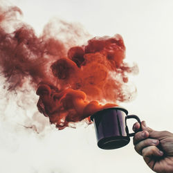 Close-up of person holding coffee cup with smoke over white background