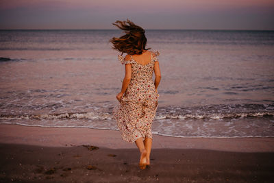 Rear view of young woman standing at beach during sunset