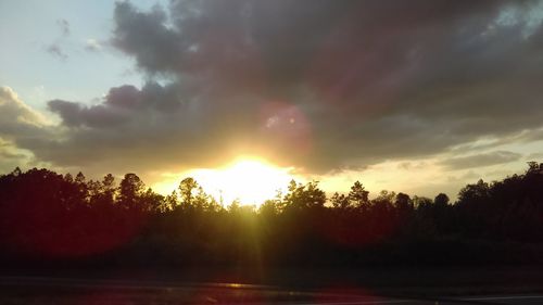 Trees on landscape against sunset sky