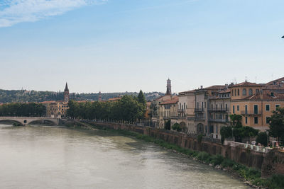 Bridge over river by buildings in town against clear sky