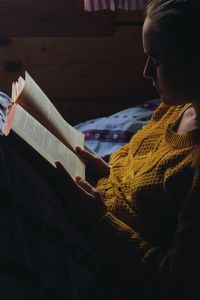 Woman reading book on bed in wooden cottage