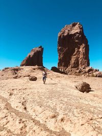 Man standing on rock against clear blue sky