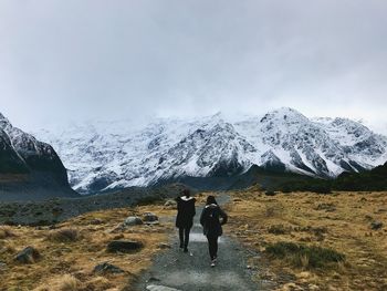 Rear view of people walking on snowcapped mountain against sky