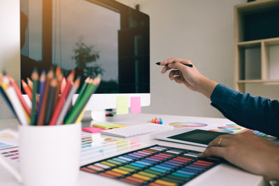 Close-up of design professional pointing at computer with color swatch on table 