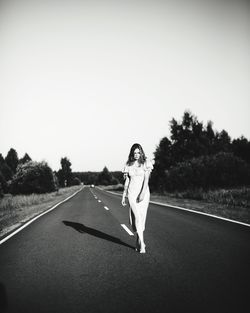 Portrait of woman walking on road against clear sky