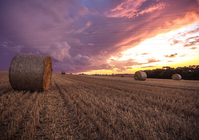 Hay bales on field against cloudy sky at sunset