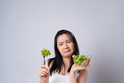 Portrait of woman holding ice cream against white background