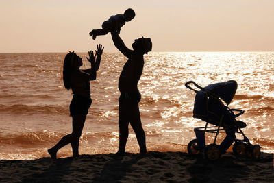 Silhouette family at beach against sky during sunset