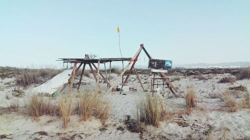 Abandoned wooden structure at sandy beach against clear sky