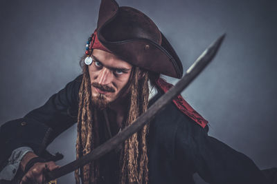 Portrait of young man in costume holding sword against gray background