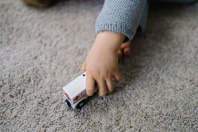 Crop little boy lying on carpet and playing with toy car in living room at home