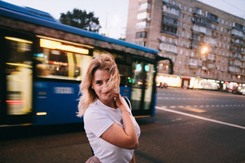 Portrait of woman with tousled hair standing on street in city at dusk