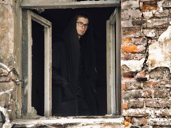 Portrait of teenage boy looking through abandoned building window