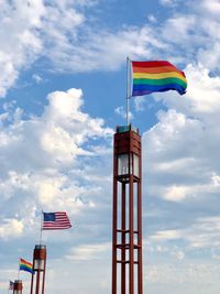 Low angle view of rainbow flags and american flag waving against cloudy sky