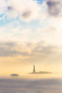 Statue in sea against cloudy sky