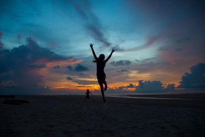 Silhouette man with arms raised on beach against sky during sunset