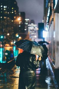 Rear view of man walking on wet street at night