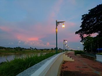 Road by canal against sky at sunset