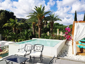 Chairs and table by swimming pool against sky