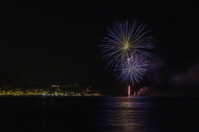 Firework display over sea against sky at night