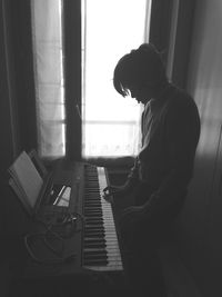 Side view of silhouette boy playing piano while standing at home