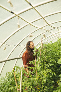 Young farmer with eyes closed smelling plants in greenhouse