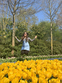 Full length of woman jumping with arms raised against flower plants