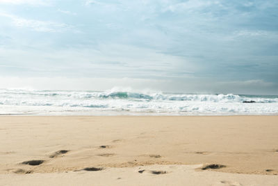 View of sandy beach with waves crashing. tranquil scene of empty beach and cloudy sky