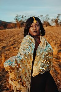 Portrait of fashion model wearing shiny scarf and jewelry standing on field