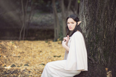 Side view portrait of fairy elf young woman sitting by tree during autumn