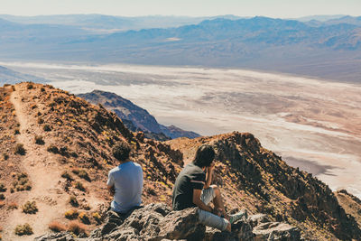 Rear view of people sitting on mountain against sky