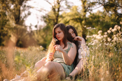 Thoughtful lesbian couple sitting in field of flowers in forest