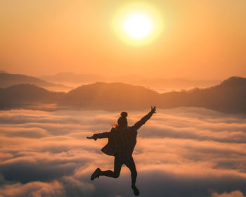 Rear view of man with arms raised standing on mountain against sky during sunset