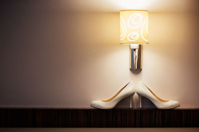 Close-up of illuminated electric lamp on table against wall