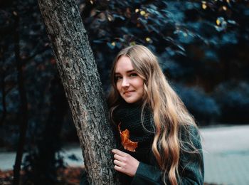 Portrait of beautiful young woman against tree trunk