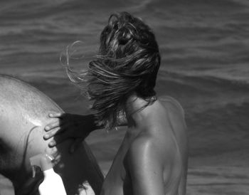 Side view of naked woman applying sun screen on man at beach