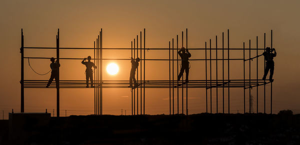 Silhouette engineers working at construction site against sky during sunset