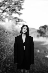 Portrait of young woman standing against trees