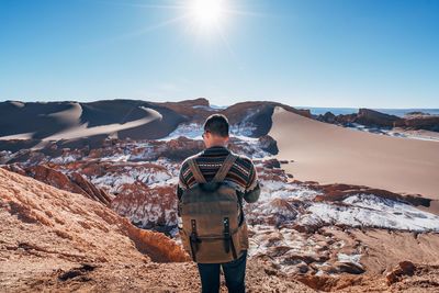 Rear view of young man with backpack standing on mountain against clear sky