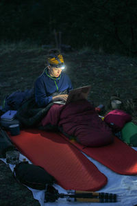 Woman using laptop while camping on field at dusk